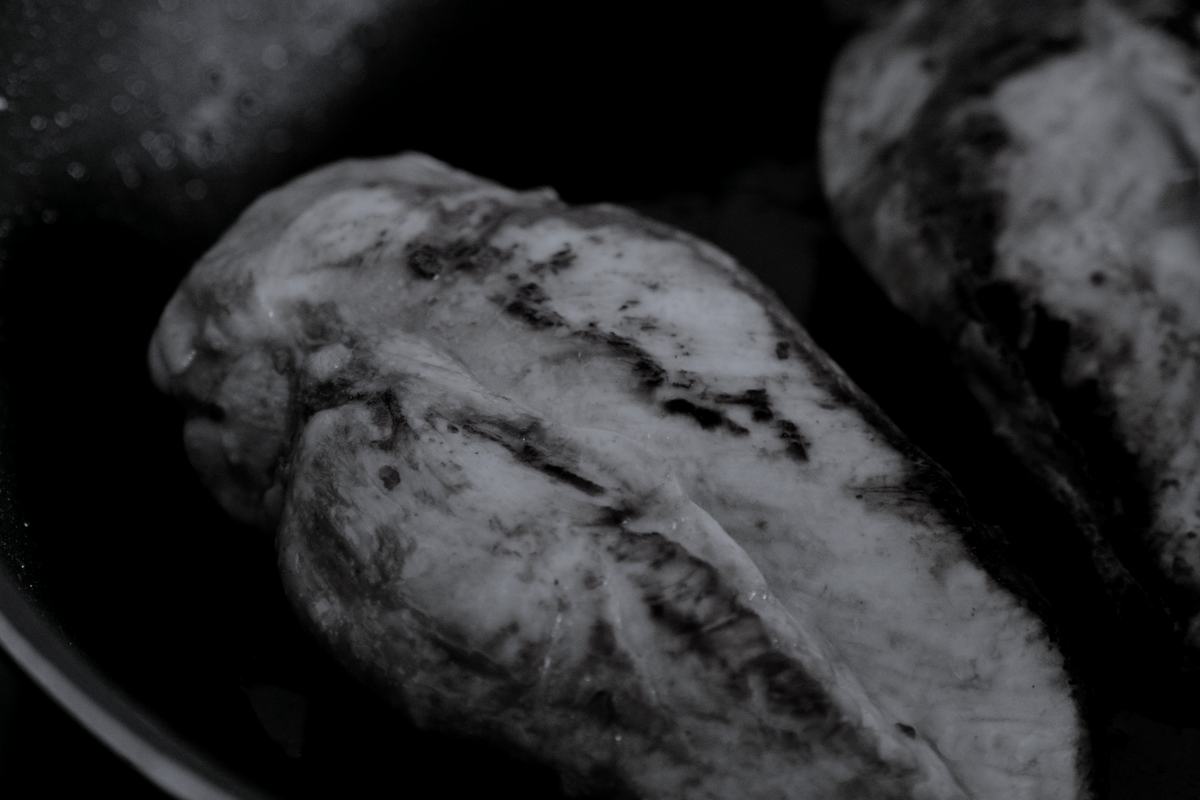 Two chicken breasts searing in a heavy pan, shot close.