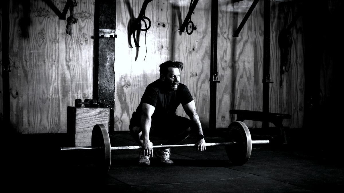 A lifter crouched over a loaded barbell in a dim, wood-walled gym.