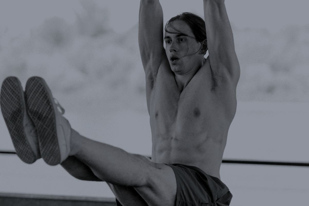 A man performing a hanging leg raise from a bar outdoors.