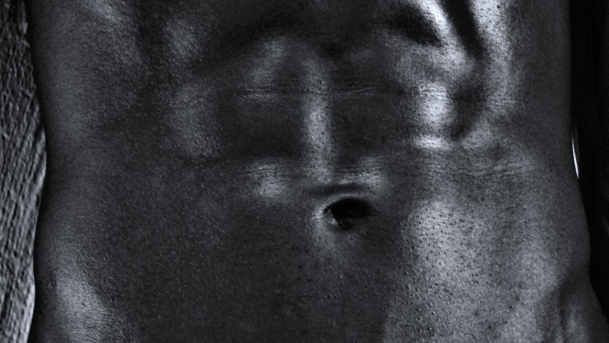 A muscular male torso in near-monochrome, lit hard from one side.