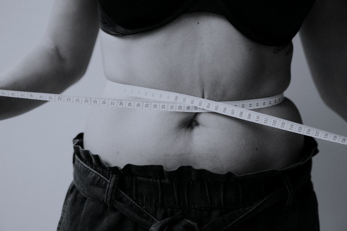 A tape measure drawn around a waist over a plain background.
