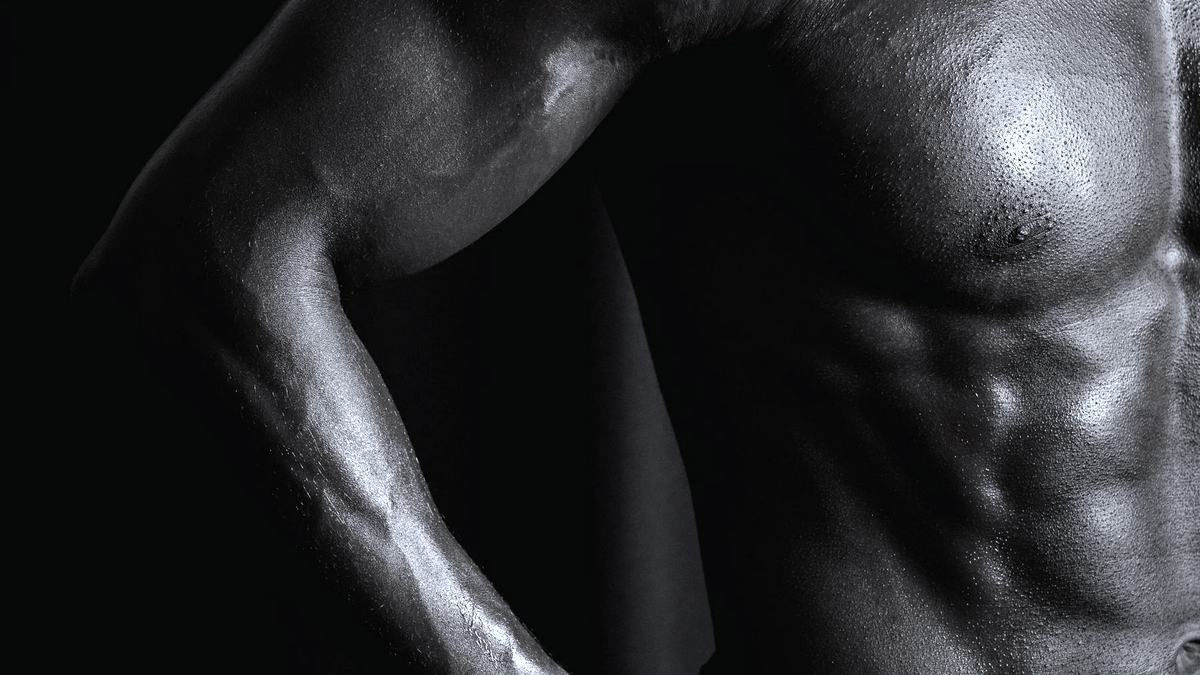 A muscular torso lit from one side against a dark background, in near-monochrome.