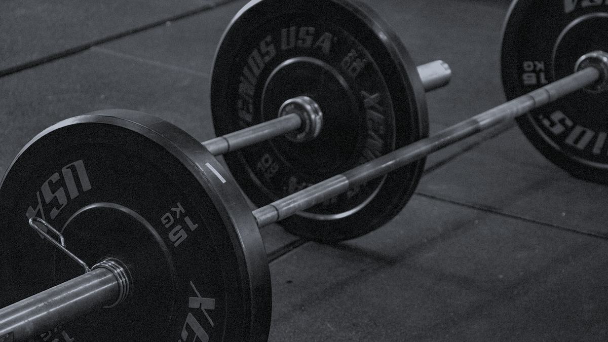 Two loaded barbells on a gym floor, bumper plates in close focus, in near-monochrome.