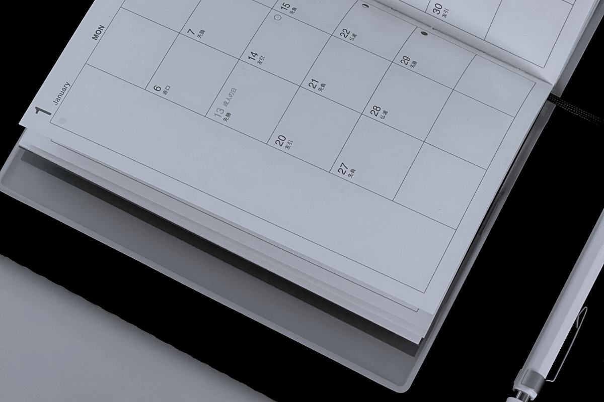 An open paper planner with a blank monthly grid and a pen resting on it.