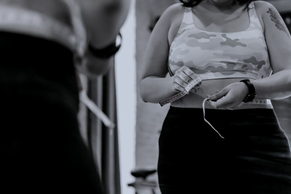 A person measuring their waist with a tape measure in a gym.
