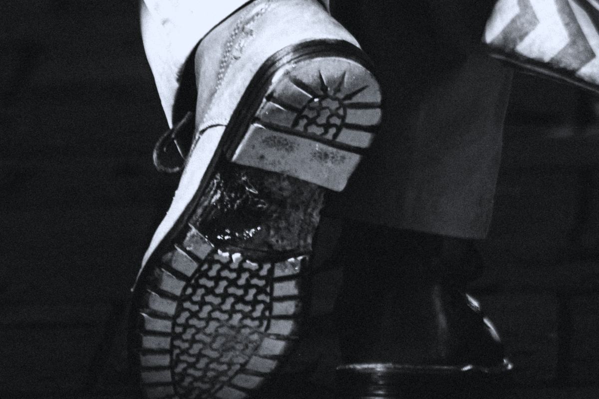 A close view of a walking shoe mid-stride on pavement, in near-monochrome.