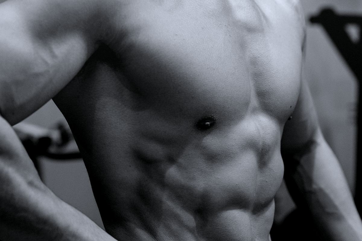 A lean, muscular torso in a gym, shot in near-monochrome.