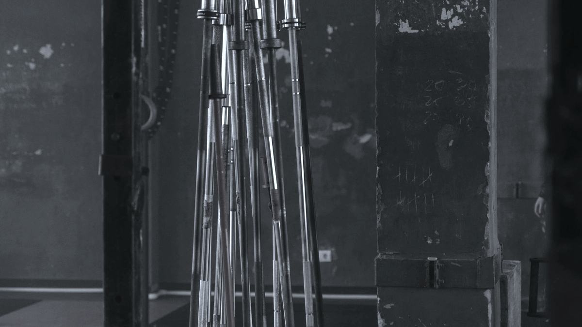 A stand of barbells against a scuffed concrete pillar with chalk tally marks on it.