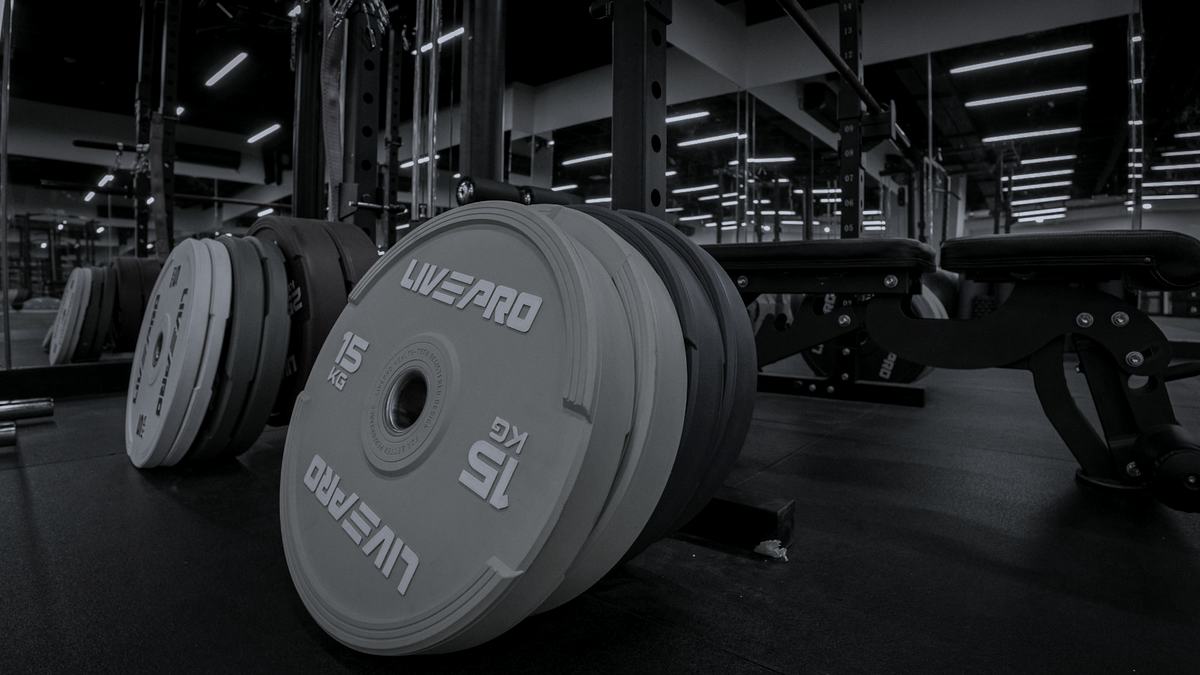 Bumper plates stacked on the floor beside a rack in an empty gym, in near-monochrome.