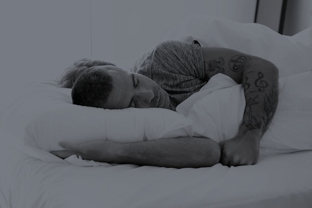 A man with tattooed arms asleep in bed.