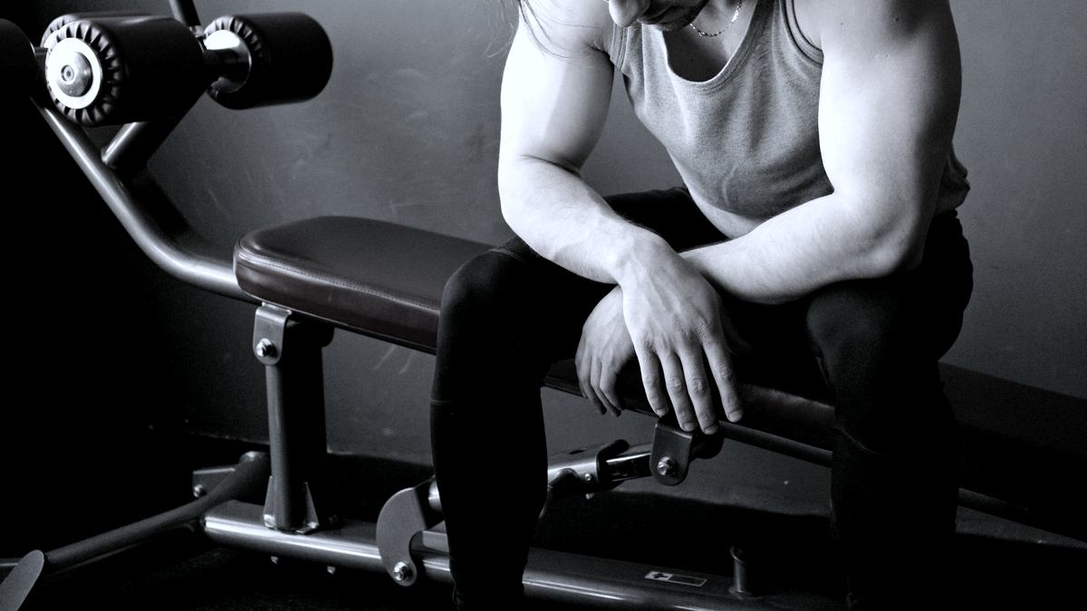 A lifter sitting on a gym bench with their head down after a set.