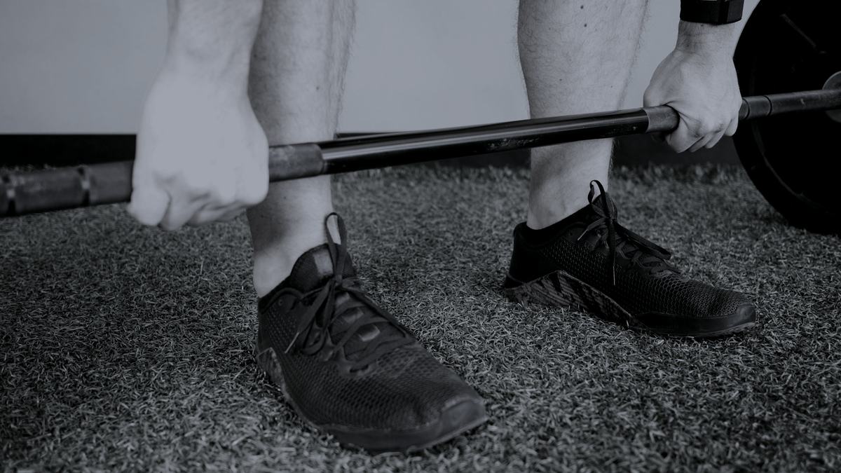 A lifter's hands set on a barbell at the start of a pull, shot low in near-monochrome.